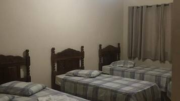 A room with three wooden beds, each with a plaid bedspread, a ceiling fan, and a light fixture.
