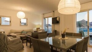 A modern living room with a dining area, large windows, and a view of the sea. - Casa Hayman        . (Ventorros de San José)