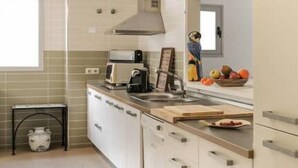 A compact kitchen with white cabinets, a built-in oven, a microwave, and a sink. There is a small window providing natural light and a fruit bowl on the counter. - Casa Hayman        . (Ventorros de San José)