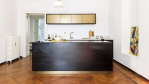 A modern kitchen with a black island, white walls, and a large abstract painting on the wall. - Macchi Master Guest apartment (Milan)