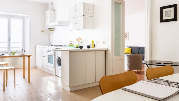 A modern kitchen with white cabinets, a built-in oven, and a dining area with a table and chairs. - Siri Master Guest apartment (Milan)