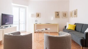 A modern living room with a flat-screen TV, a grey sofa, a small round table, and a desk with a lamp. - Siri Master Guest apartment (Milan)