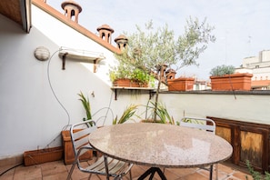 A round table with metal chairs, a potted plant, and a wall-mounted light fixture.