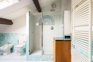 A bathroom with a shower, bidet, toilet, and a wooden cabinet.