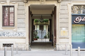 An entrance with a wrought iron gate, a small balcony with plants, and a building facade with a sign.