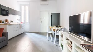 A modern kitchen with white cabinets, a grey sofa, and a dining area with a white table and chairs. - Anfossi Master Guest apartment (Milan)