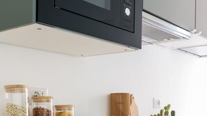 A modern kitchen with a built-in microwave, wooden cutting board, and jars of grains and beans on the counter. - Anfossi Master Guest apartment (Milan)