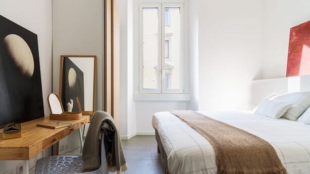 A bedroom with a bed, a desk with a chair, a window, and a painting on the wall. - Anfossi Master Guest apartment (Milan)