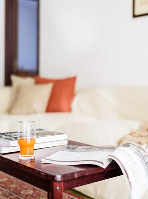 A living room with a coffee table holding a glass of orange juice, a magazine, and a book. A white sofa with an orange pillow is in the background. - Orobie Master Guest apartment (Aprica)