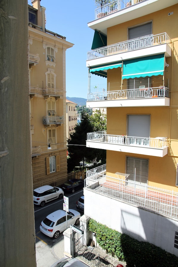 A multi-story building with balconies, a street with parked cars, and a clear sky.