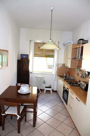 A small kitchen with a dining table and chairs, a window with blinds, and basic appliances.
