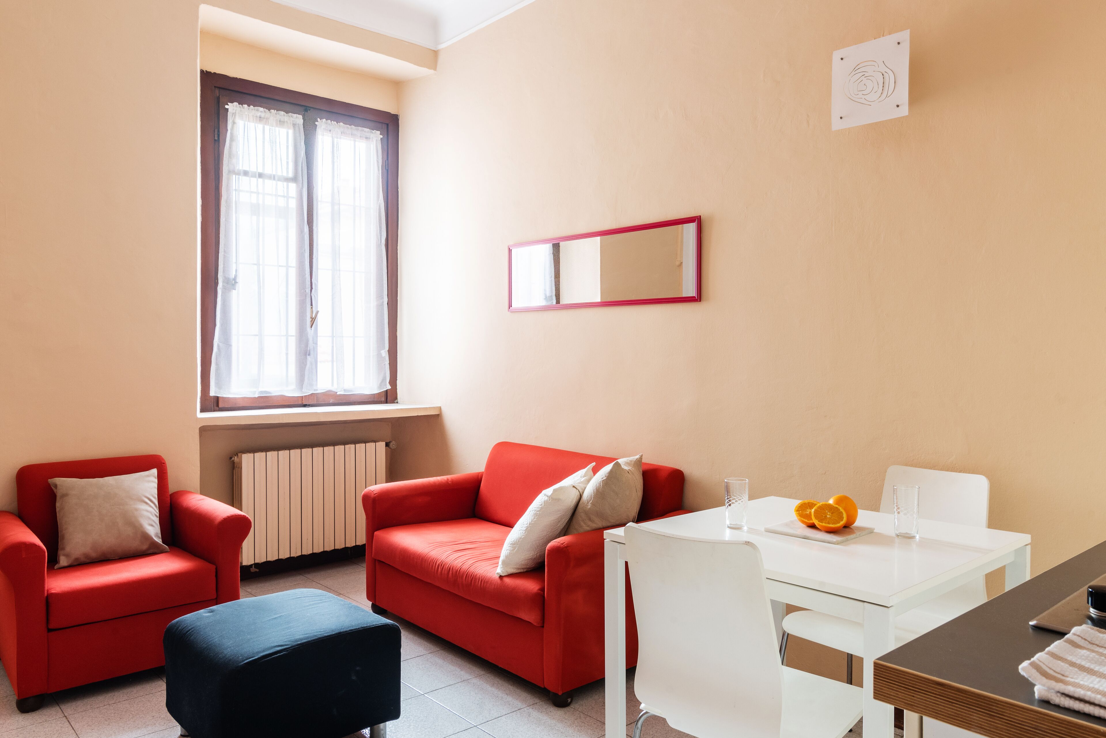 A room with a red sofa, a white table, and a window with curtains.