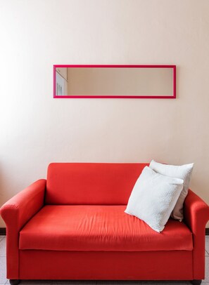 Un sofá rojo con un cojín blanco frente a una pared con un espejo de marco rojo.