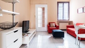 A modern living room with a TV, red sofas, a white table, and a window with curtains. - Asso Master Guest apartment (Milan)