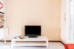 Un mueble blanco para televisor con un televisor Samsung, una revista y una silla roja en un rincón de una habitación con una pared color beige y una ventana.