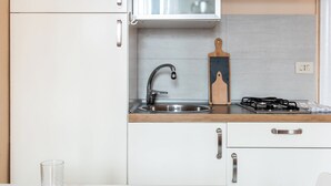A modern kitchen with white cabinets, a stainless steel sink, and a gas stove. There is a cutting board and a glass on the countertop. - Asso Master Guest apartment (Milan)