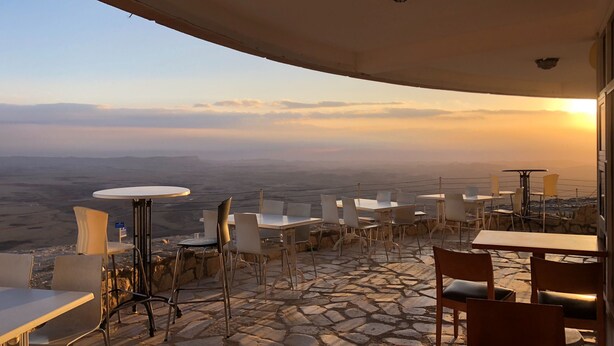 Une terrasse extérieure, dotée de tables et de chaises, qui offre une vue sur un paysage montagneux au coucher du soleil.