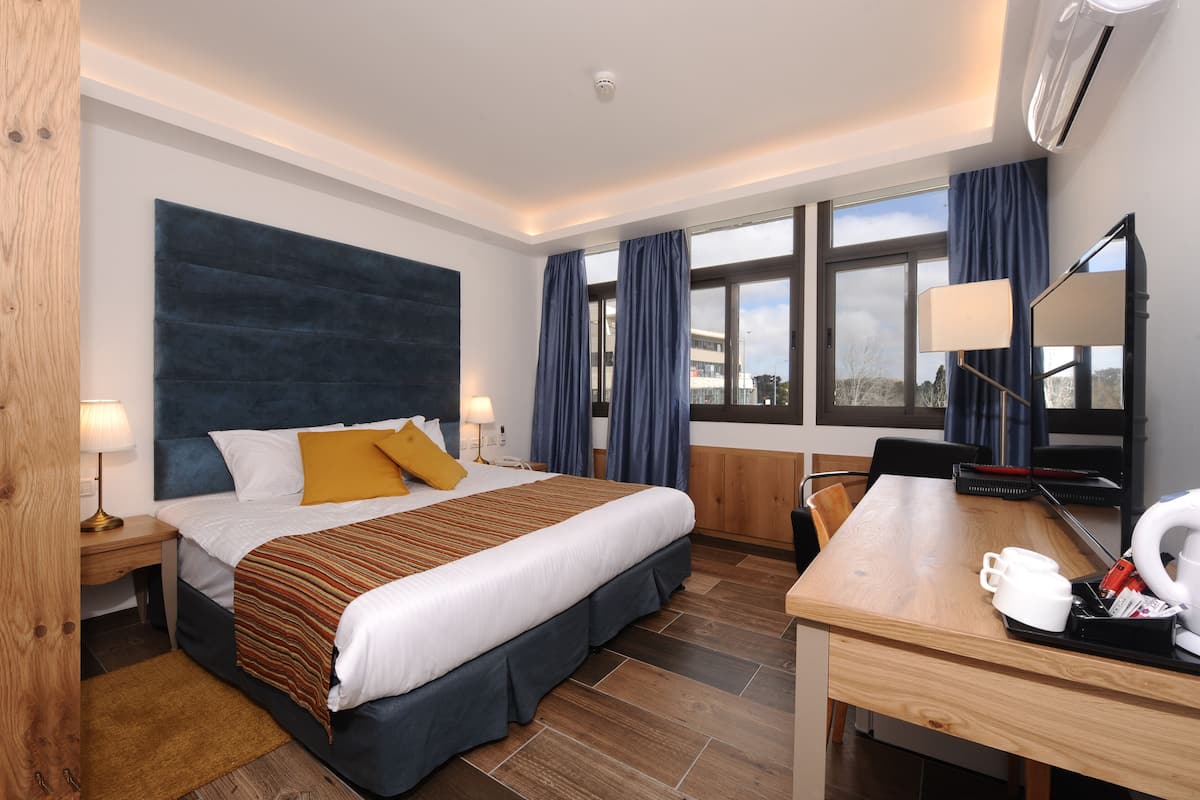 Une chambre d’hôtel équipée d’un lit, d’un bureau, d’une chaise, d’une lampe, d’une machine à café et d’une fenêtre avec des rideaux.
