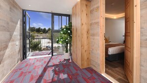 Une chambre moderne dotée d’une grande porte-fenêtre coulissante donnant sur un balcon, d’une armoire en bois et d’un lit avec une tête de lit.
