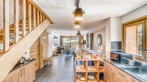 A modern kitchen with wooden cabinetry, a built-in stove, and a dining area with a long table and chairs.