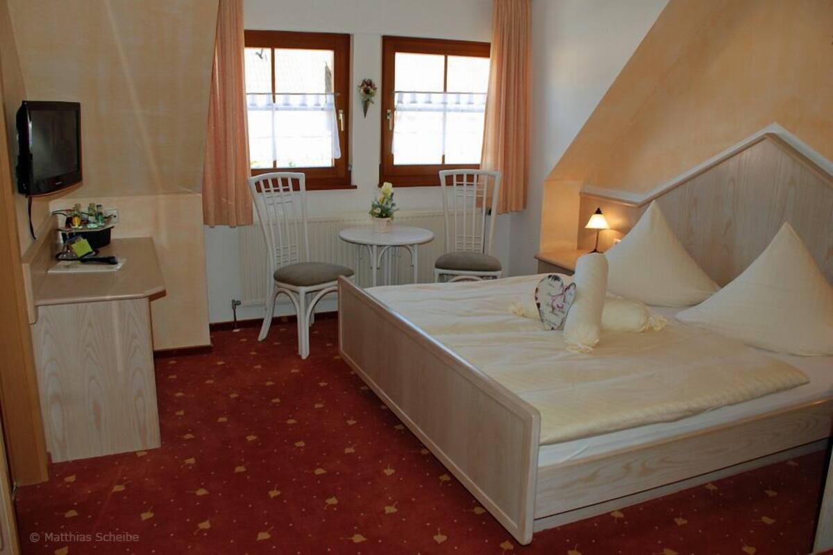 Quarto com cama, escrivaninha, cadeira, mesinha e televisão.
