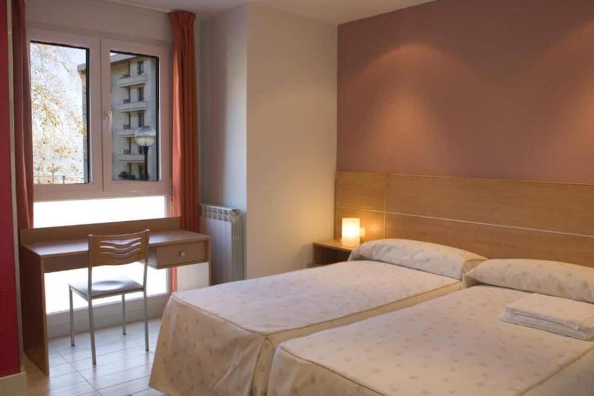 A hotel room with two beds, a desk, and a chair.