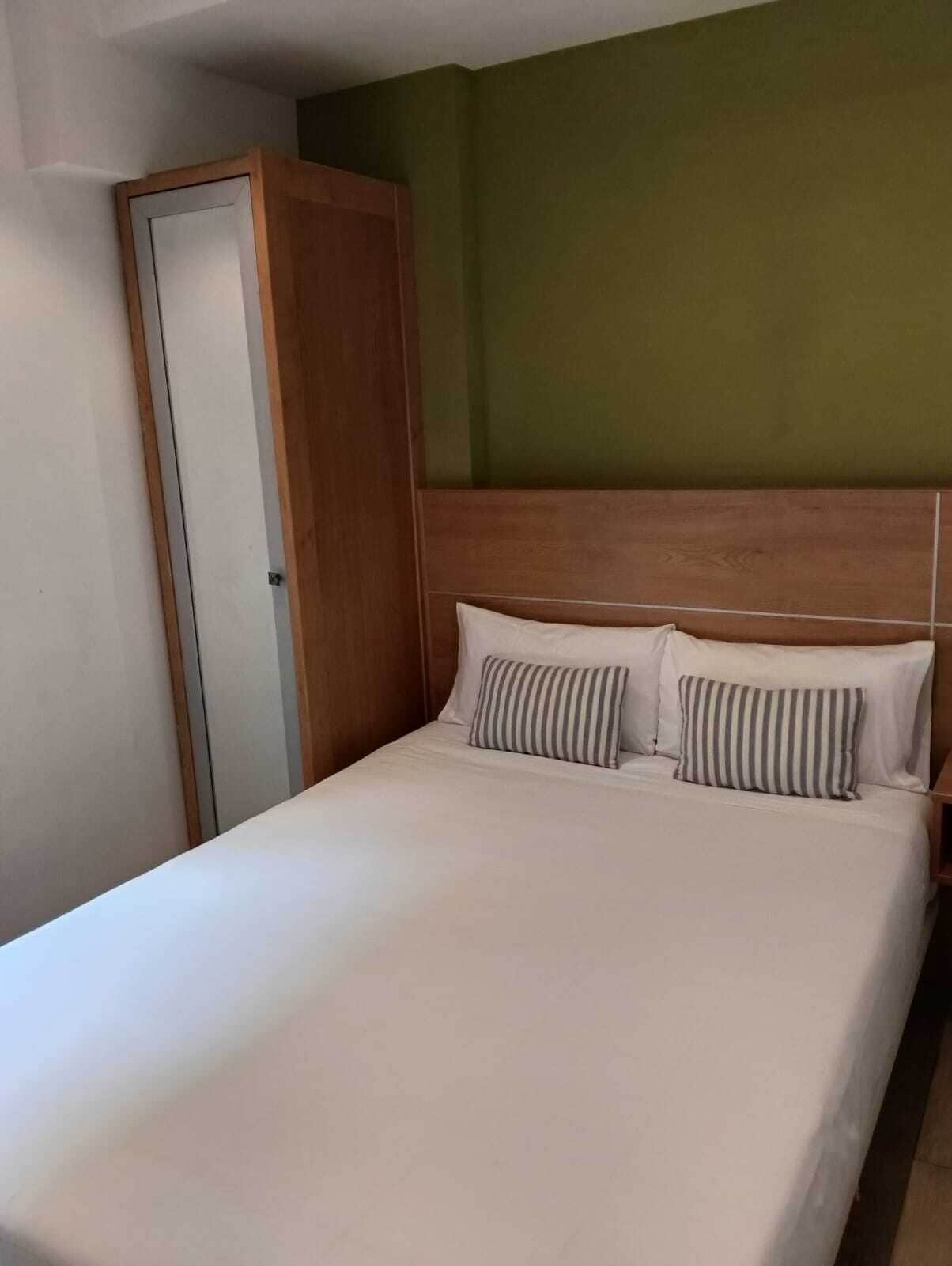 Una cama individual con dos almohadas, cabecera de madera y pared verde.