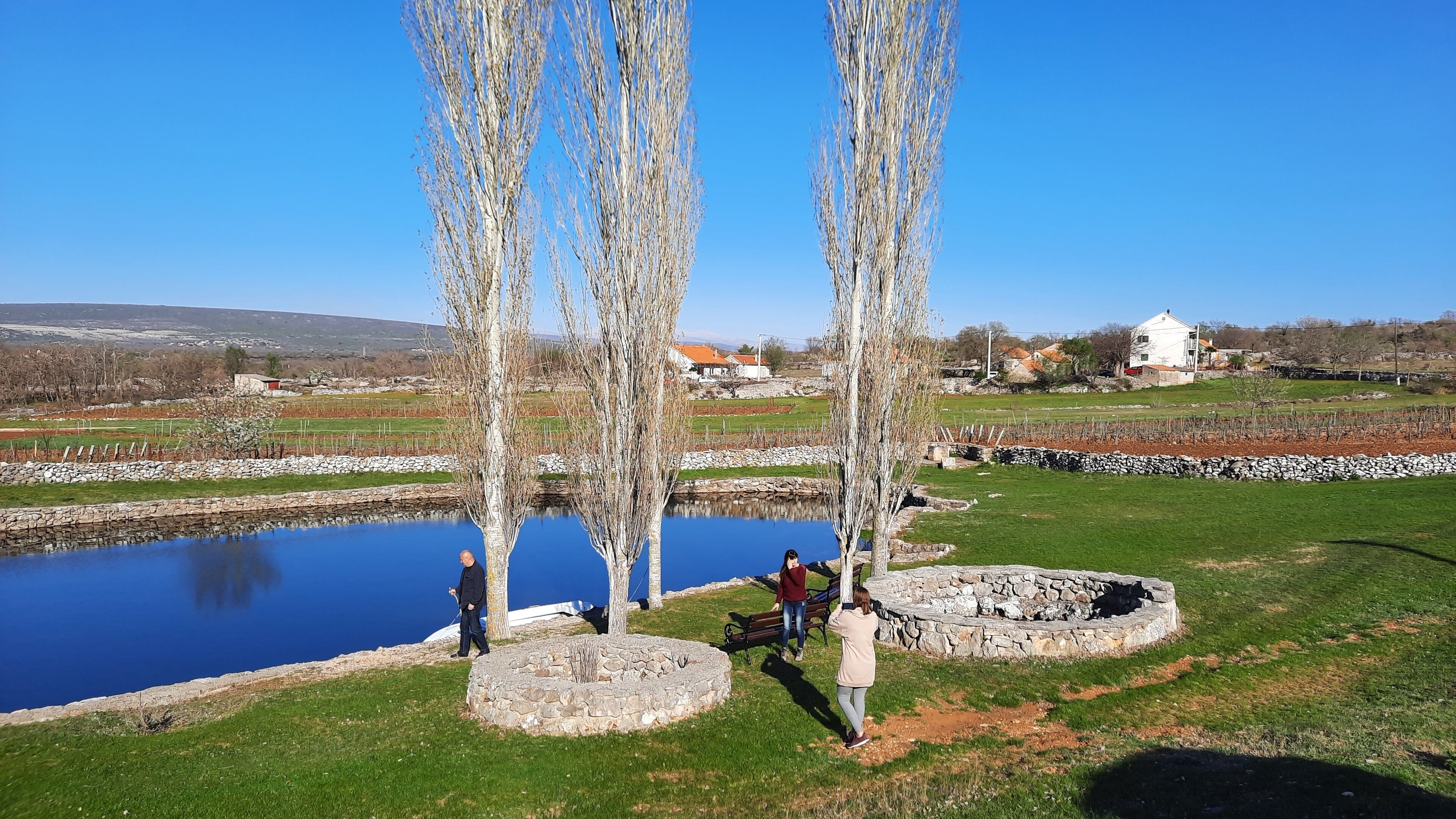 Un espace extérieur paisible, avec un étang, des constructions en pierre et un ciel d’un bleu limpide.