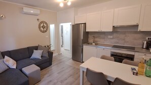 A modern kitchen with white cabinets, a stainless steel refrigerator, and a dining area with a white table and chairs. - NEW Apartment, A2+2, Family house - OPG Rudan, garden pool, terase, wi-fi (Drnis)