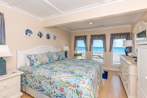 A bedroom with a bed, a dresser, a nightstand, and a view of the ocean.