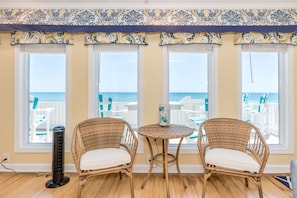 A room with three large windows, wicker chairs, a small round table, and a standing fan.