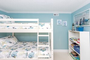 A child's bedroom with bunk beds, a bookshelf, and a painting of a beach scene.