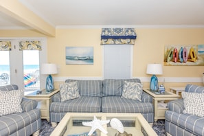 A living room with a striped sofa set, a coffee table with decorative items, and a view of the ocean through large windows.