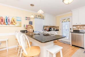 A kitchen with a central island, white cabinetry, and a dining area with chairs.