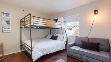 A bunk bed with a playroom rules sign, a grey sofa, and a window with blinds.