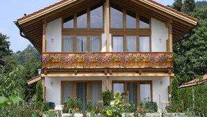 Een chalet met twee verdiepingen, een houten balkon, grote ramen en een tuin ervoor.