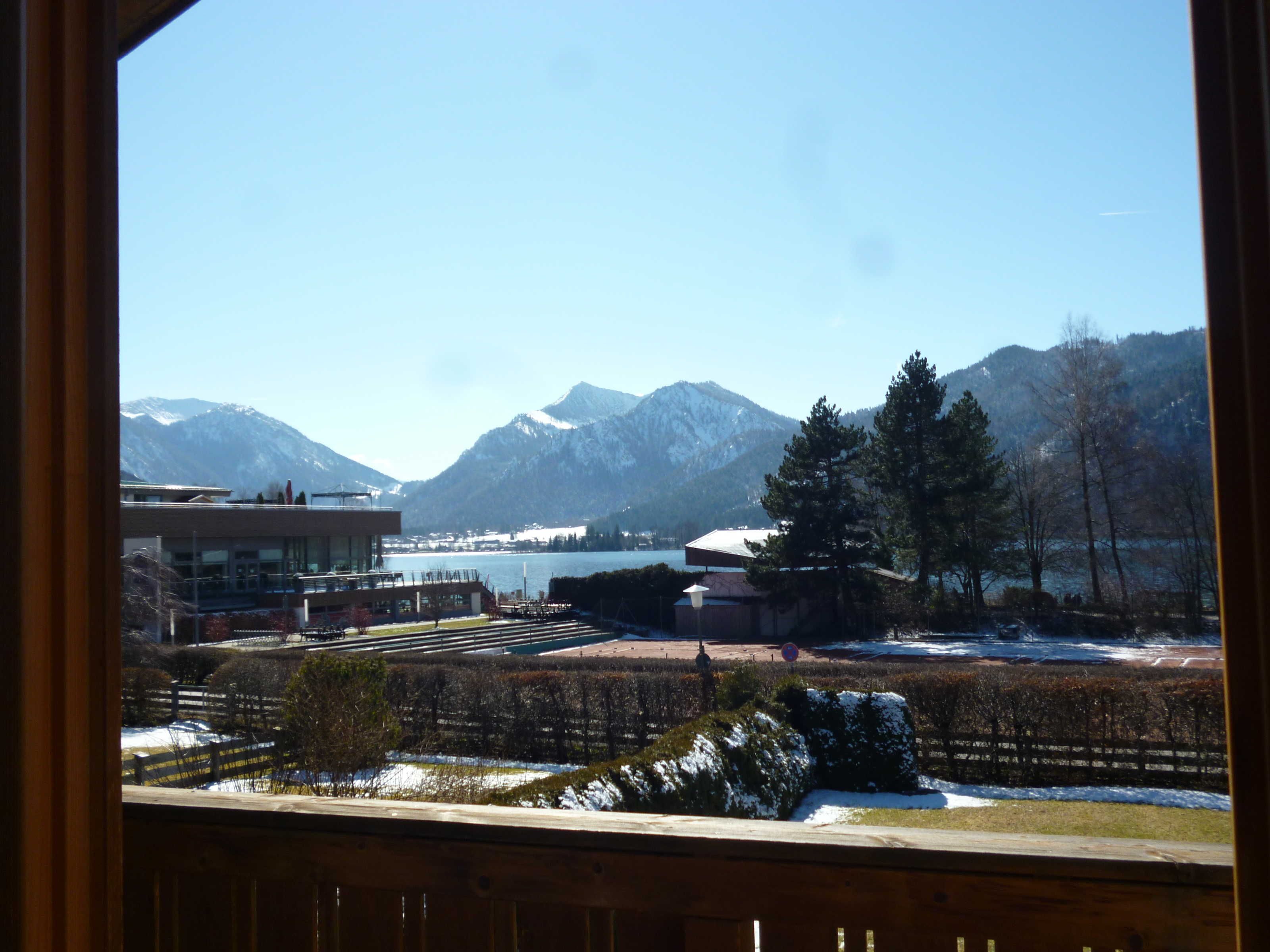 Une vue depuis une fenêtre donnant sur un paysage montagneux avec un lac, des bâtiments et un sol recouvert de neige.