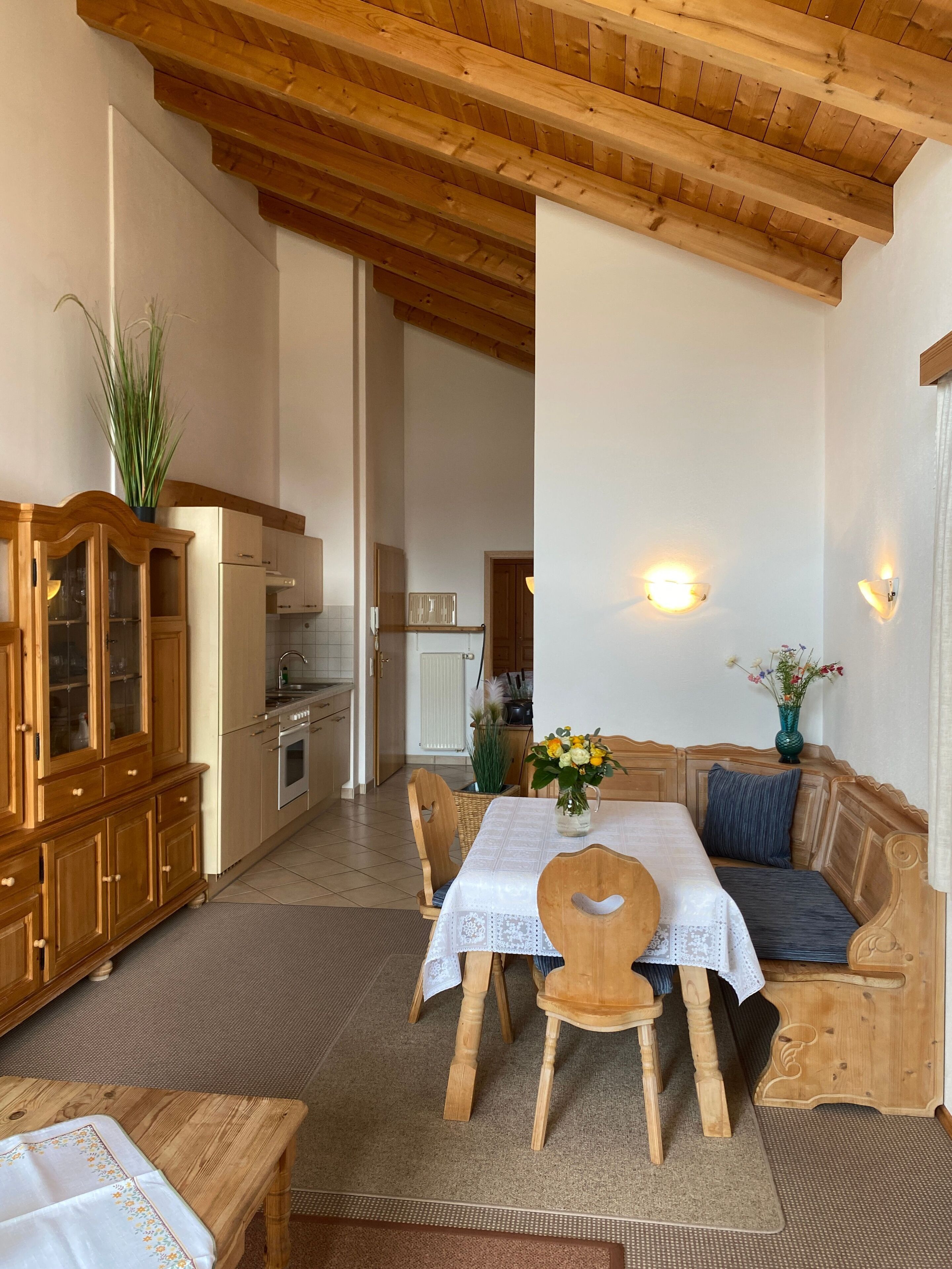 Un coin repas chaleureux, avec des meubles en bois, une table dressée pour deux personnes et une vue sur la cuisine.