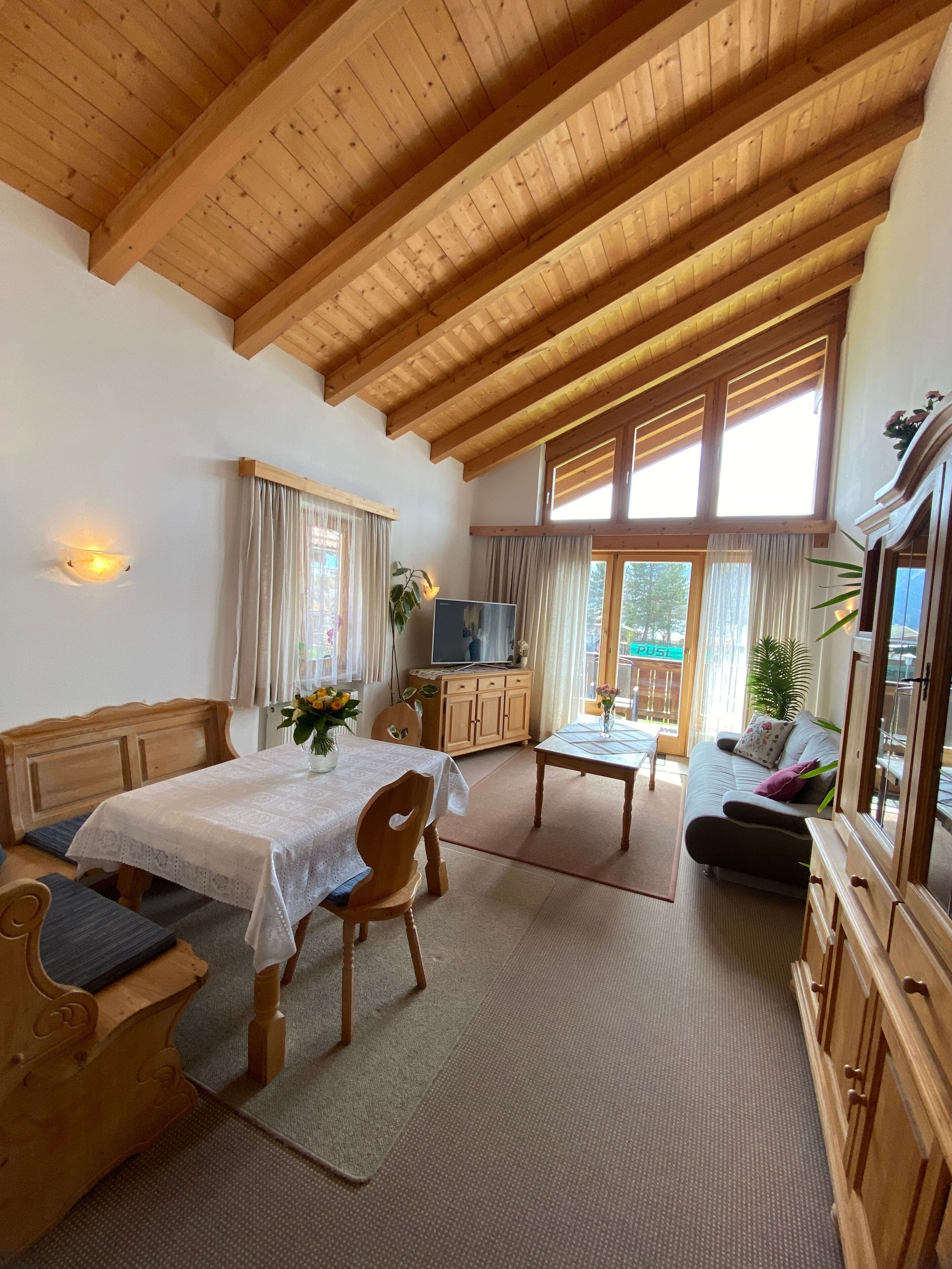 Ein gemütliches Zimmer mit Holzboden, einem Bett, einer Couch, einem Esstisch und einem Fernseher.