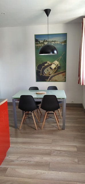 A dining area with a table, two chairs, a pendant light, and a coastal landscape painting on the wall.