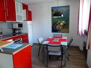 A compact kitchen with red and white cabinets, a microwave, and a dining area with a table and chairs.