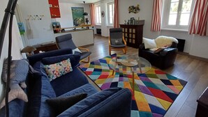 A living room with a blue sofa, a glass coffee table, and a colorful rug. There is a wooden cabinet and a chair with a star pillow. - Bright and quiet apartment 61 m2 5 minutes walk from the Port (Le Palais)