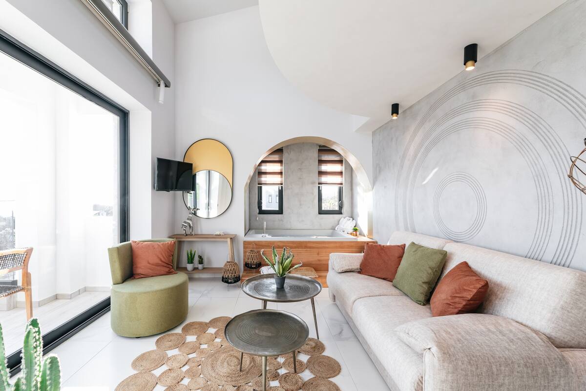 Un salon moderne avec un canapé, une table basse ronde et un téléviseur. Il y a une grande fenêtre et une vue sur la ville.