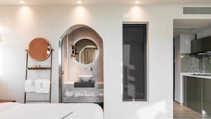 Una habitación de hotel moderna con una cama, un espejo redondo, un lavamanos y vistas a la cocina.