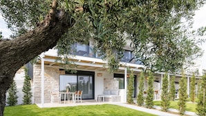 Una casa moderna con fachada de piedra, un patio con mobiliario exterior y un césped bien cuidado.