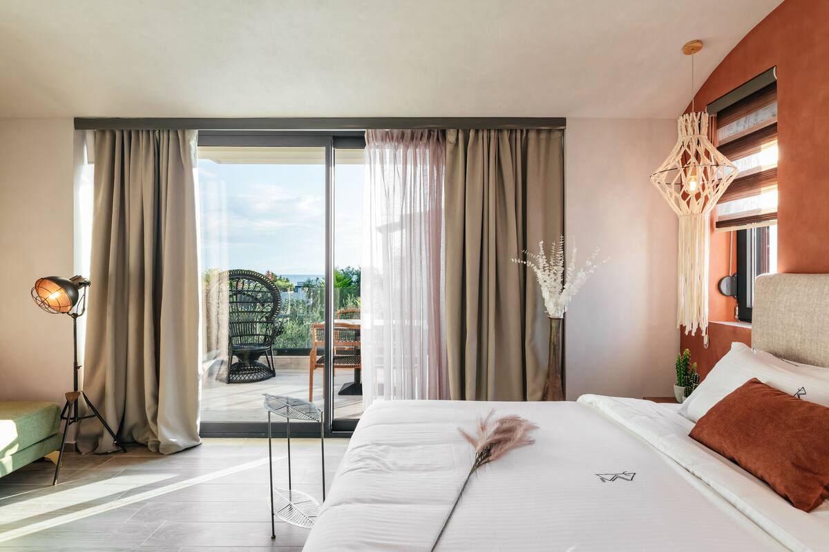 Une chambre d’hôtel avec un grand lit, une vue à travers la porte vitrée, une lampe sur pied et un luminaire suspendu.