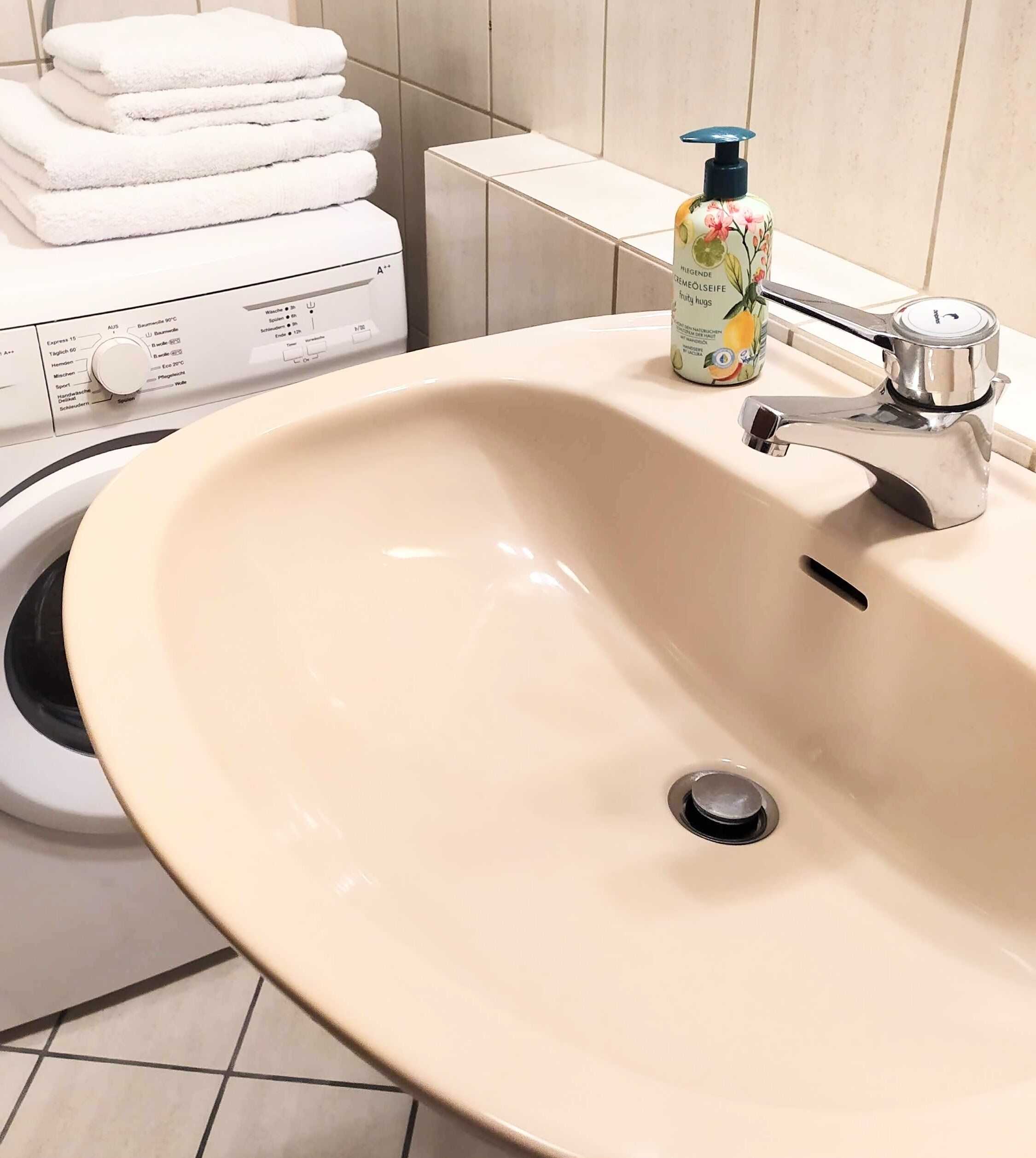 Un baño con un lavabo color crema, un grifo, un dispensador de jabón y un perchero para toallas apiladas.