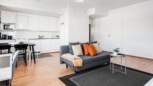 Un apartamento moderno con un sofá gris, una mesa de comedor y una zona de cocina.