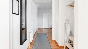 Un pasillo con un felpudo gris, paredes blancas y suelo de madera.