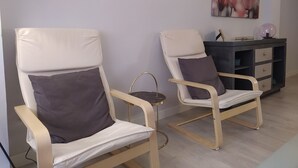 Dos sillones reclinables con cojines, una mesita redonda y un mueble oscuro con cajones.